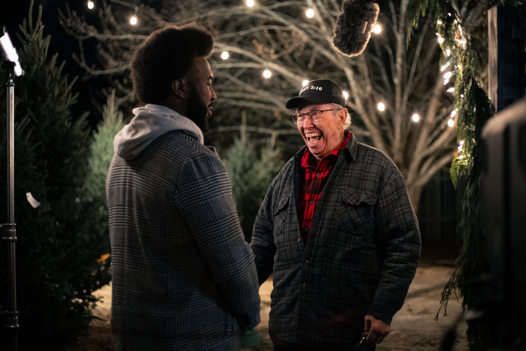 Two actors sharing a laugh under string lights