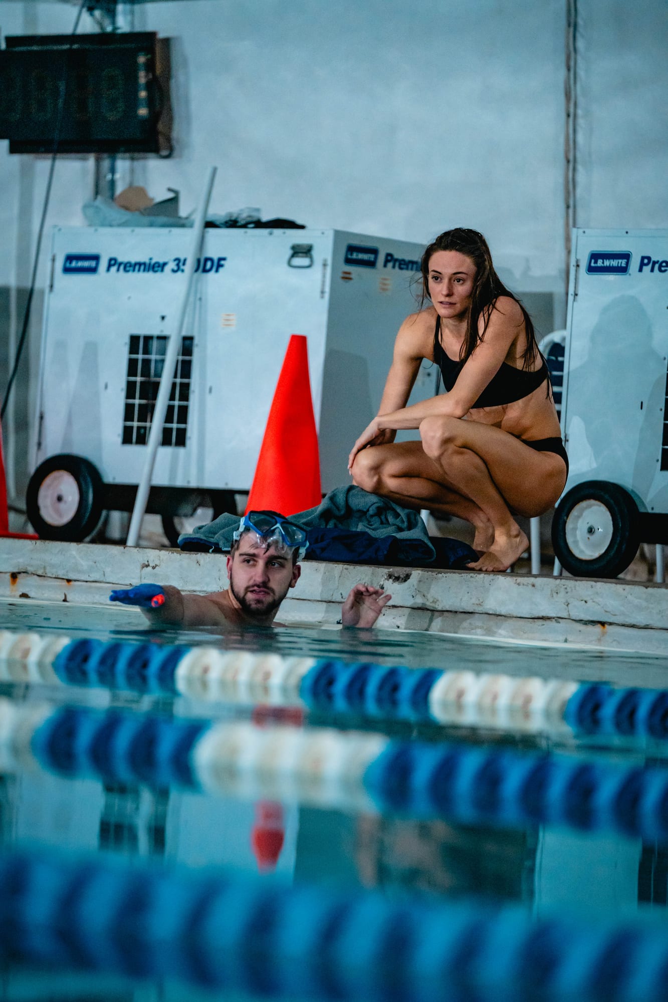 Professional swimmer crouched on pool deck between takes