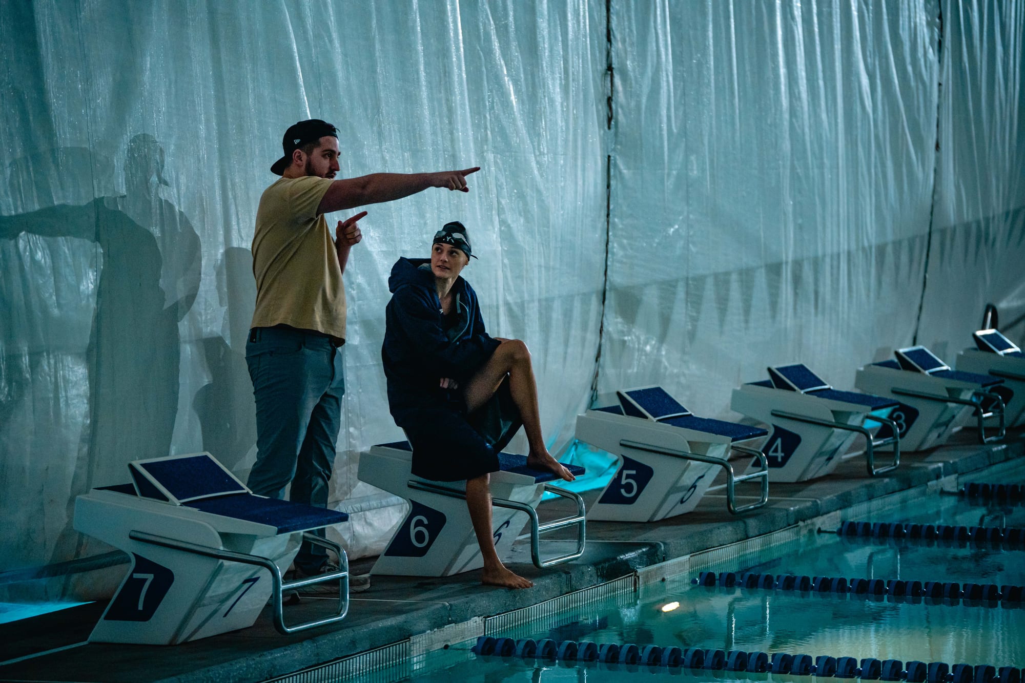 Crew member pointing direction to swimmer seated on starting block